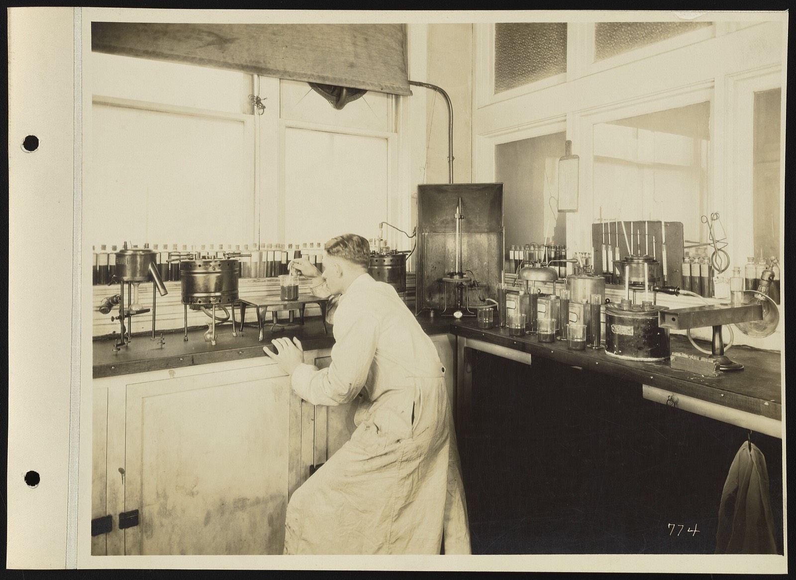A chemist in a long white coat leaning over a bench of apparatus at the Dearborn Chemical Company laboratory