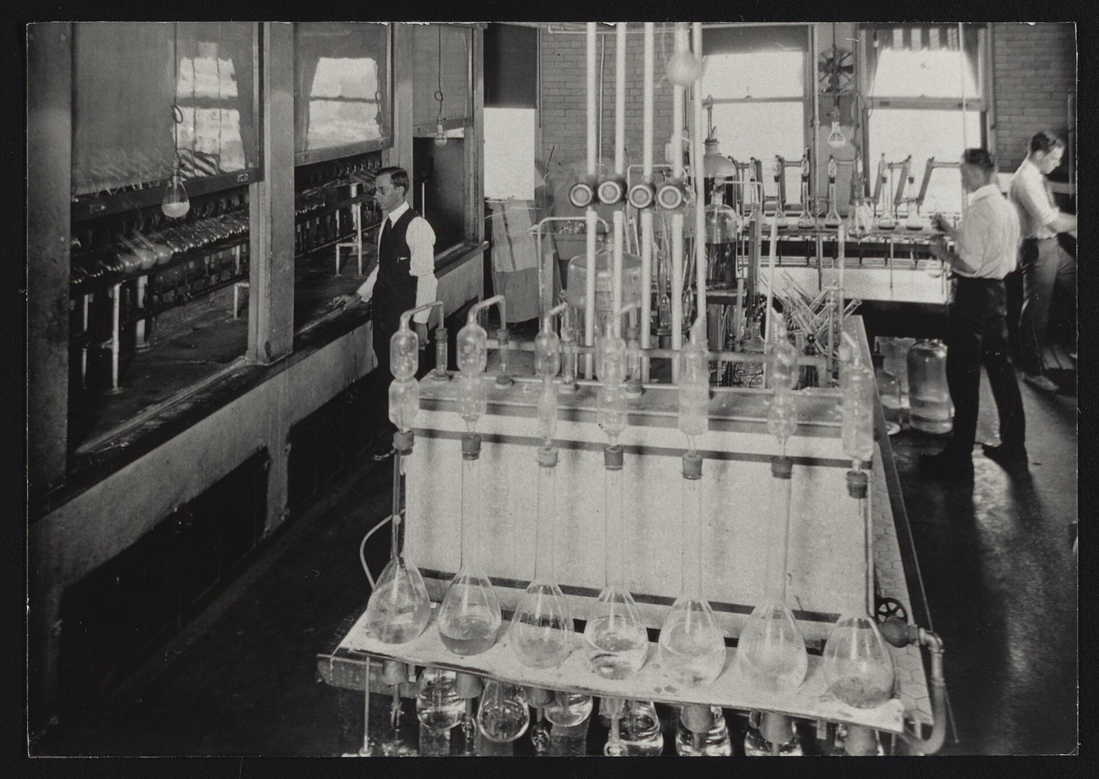 A row of gas-washing flasks on a bench with chemists working in the Bureau of Chemistry Nitrogen Laboratory, 1900s–1920s
